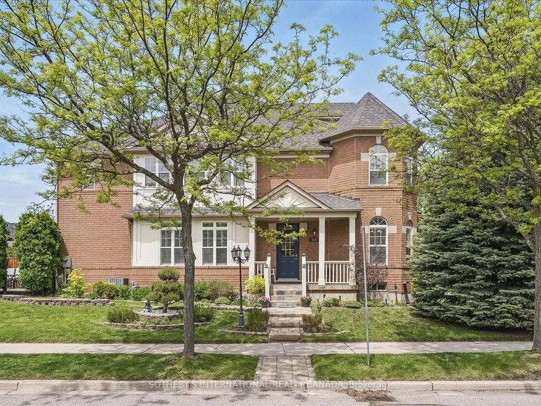Two-storey brick home with a covered front porch and navy door behind a lawn and mature trees at 220 Walkerville Road, Markham, Ontario